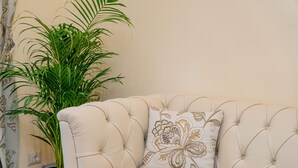 A tufted sofa with a floral pillow and a potted plant beside it.