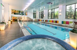 A modern indoor swimming pool with clear water, a hot tub, and a seating area with colorful cushions. - Orhideea Residence & Spa (Bucharest)