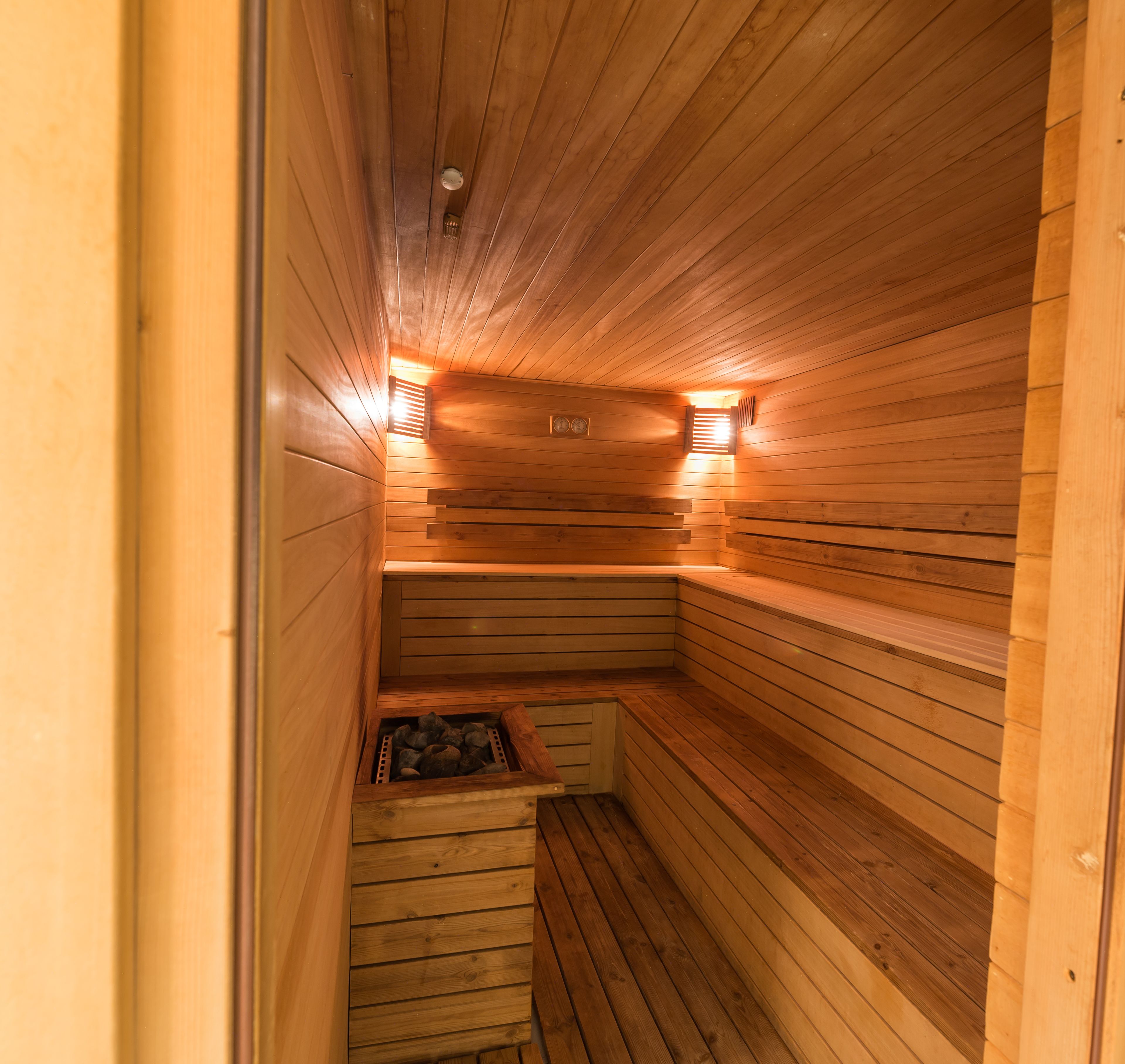 Una sauna con paredes y bancos de madera, techo inclinado y dos luces fijadas a la pared.