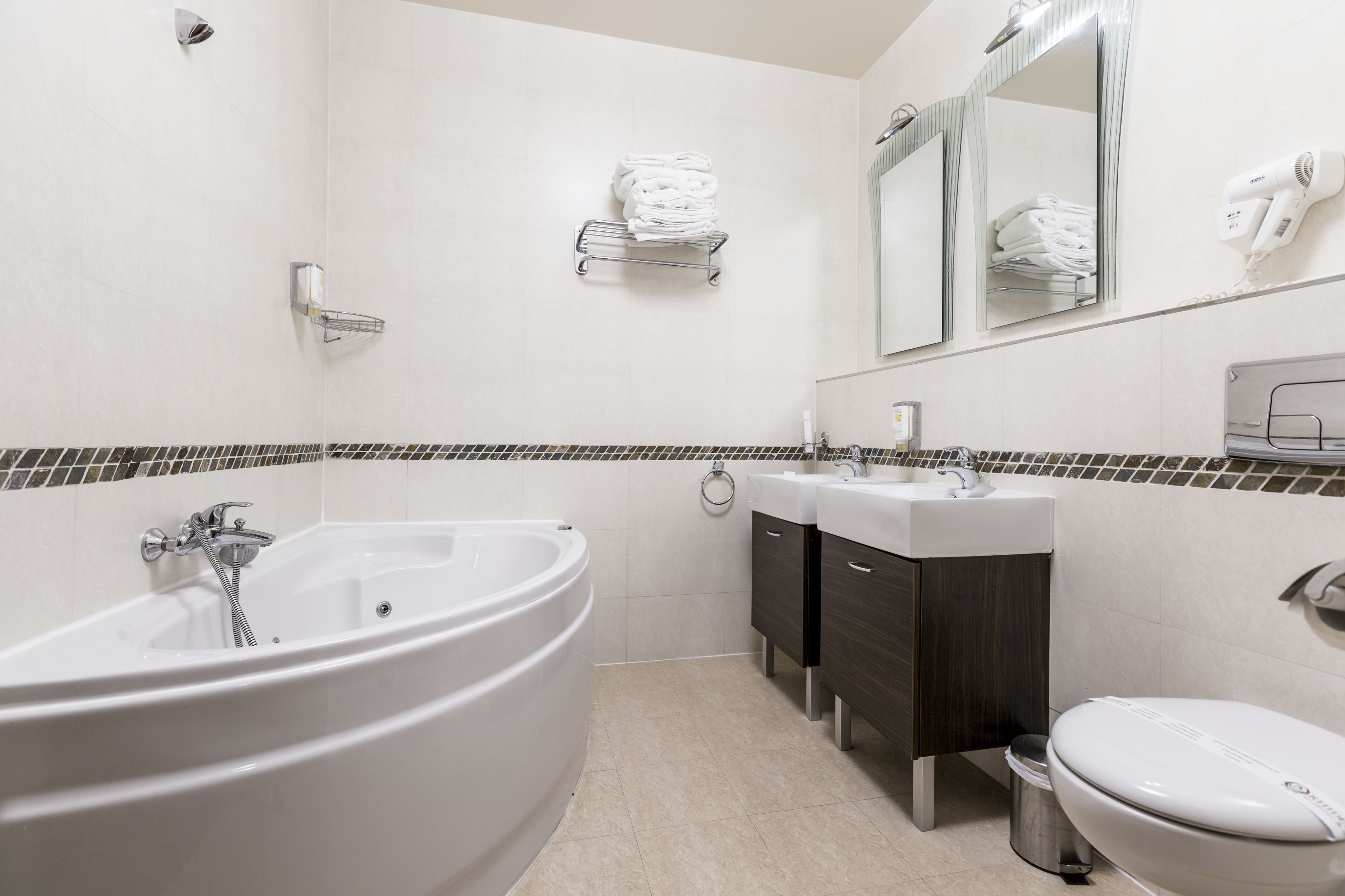 Ein modernes Badezimmer mit einer großen Badewanne, zwei Waschbecken, einer Toilette und einem Handtuchhalter.
