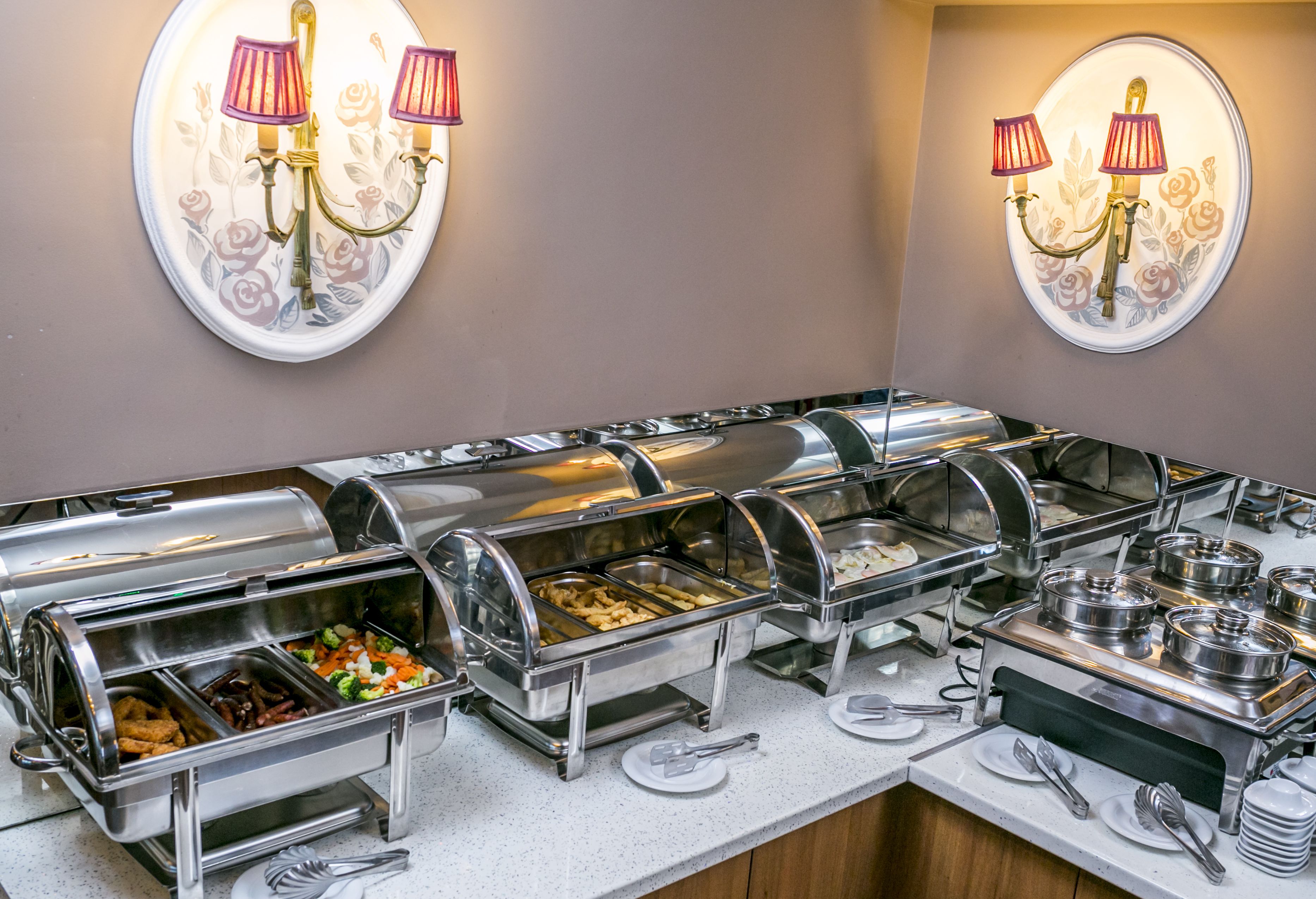 Un espace buffet comprenant plusieurs stations de service où les clients peuvent se servir eux-mêmes, avec différents plats présentés sur des plateaux et une variété d’ustensiles à disposition sur le comptoir.