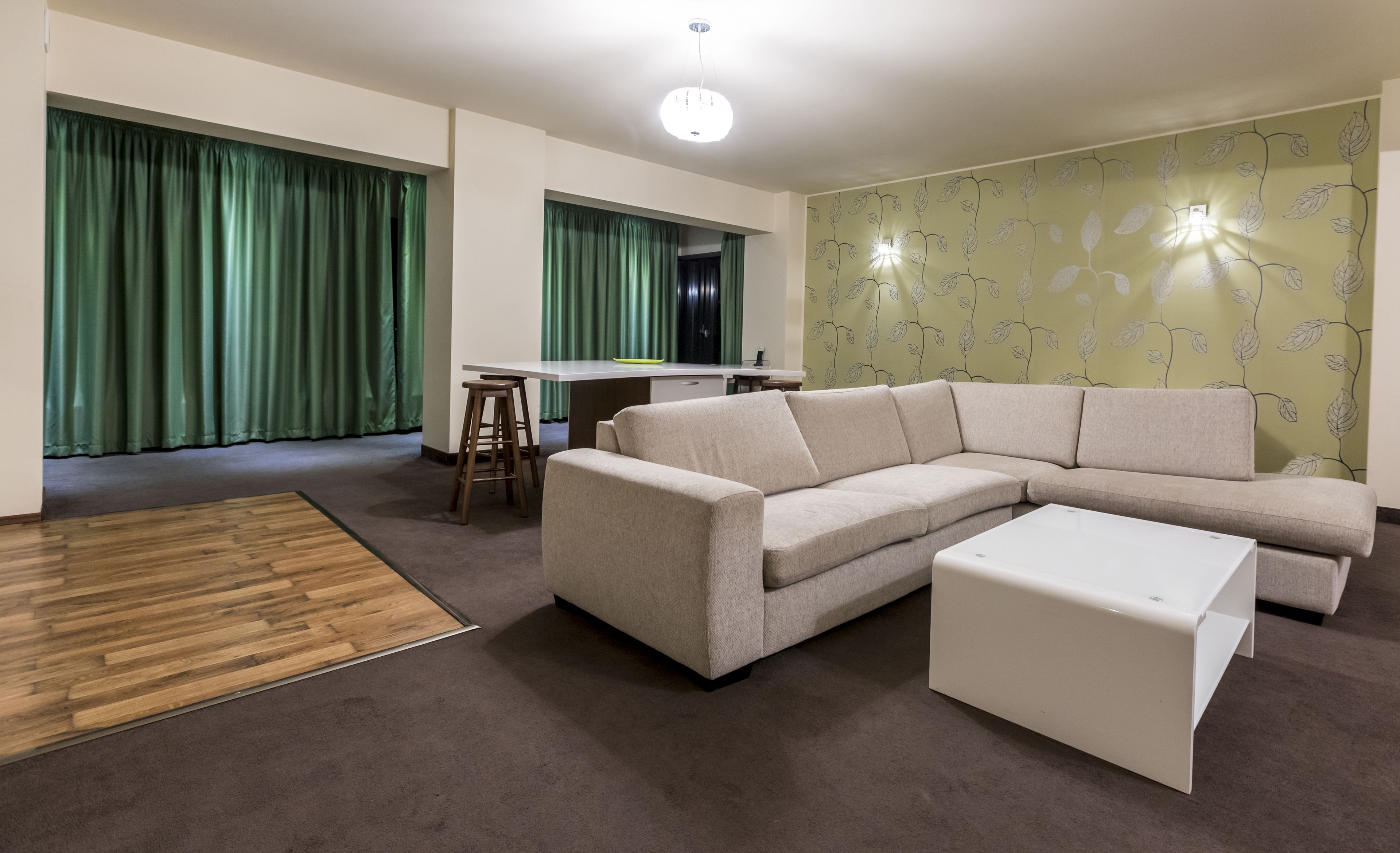 A modern living room with a beige sectional sofa, a white coffee table, and a wooden floor rug.