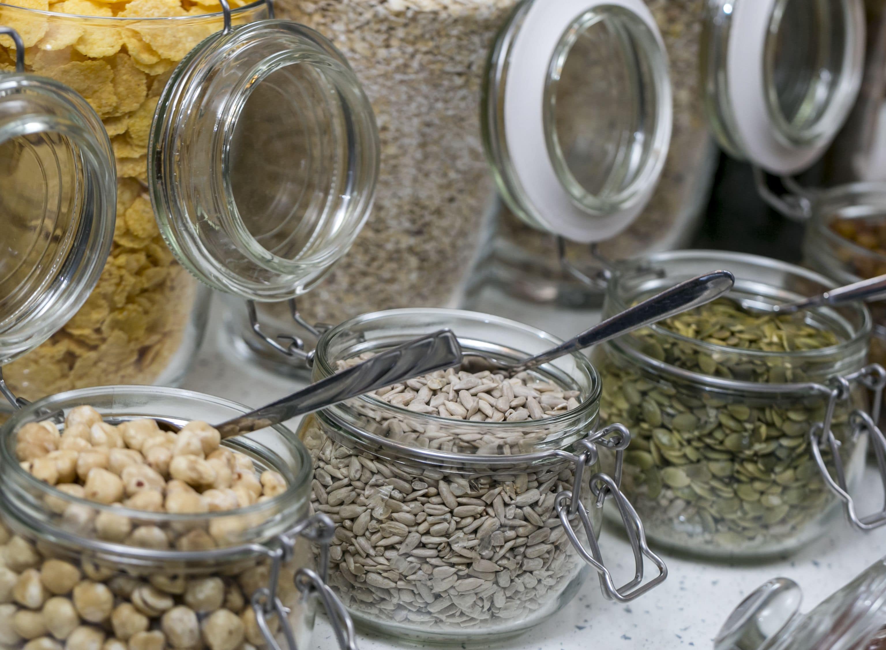 A variety of food items in glass jars with metal clasps, including sunflower seeds, chickpeas, and other grains.