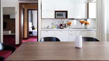 A modern hotel room with a wooden dining table, a white vase with flowers, a microwave, and a sink in the kitchen area.