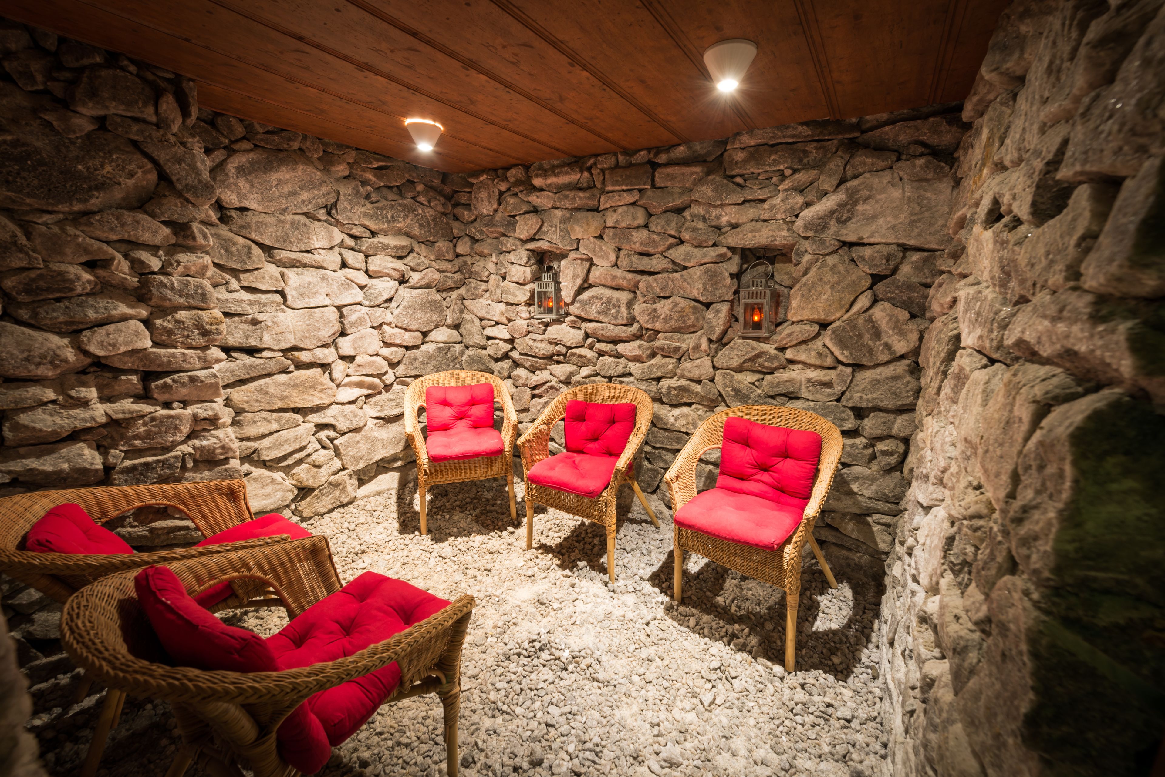 Habitación con paredes de piedra, sillas de mimbre y cojines rojos.