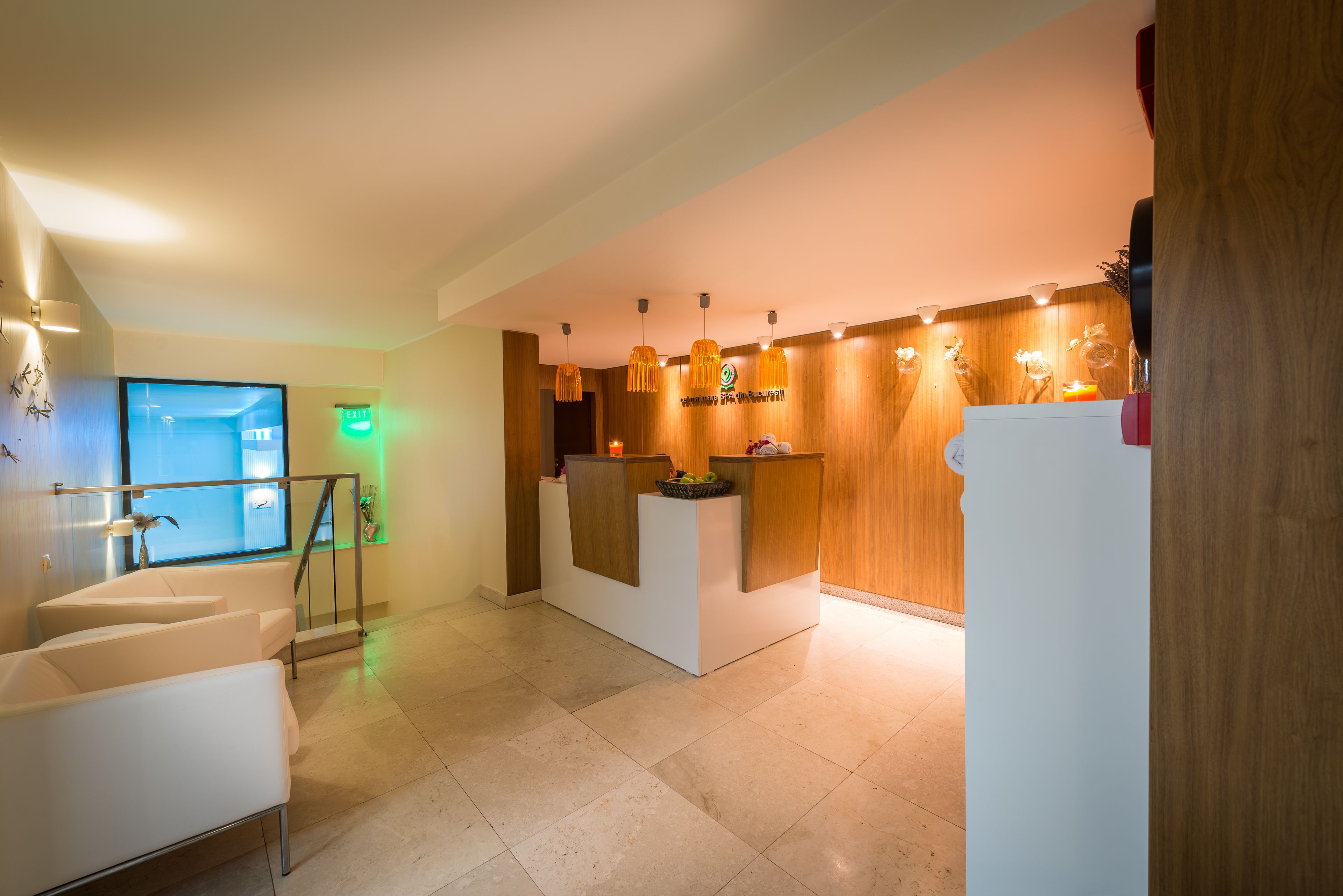 A reception area with a wooden reception desk, a glass door leading to a hallway, and a seating area with white chairs.