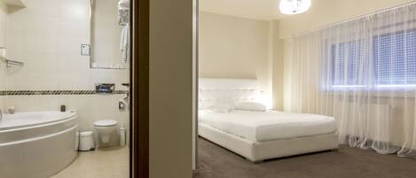 A hotel room with a large bed, a separate bathroom, and a window with sheer curtains.