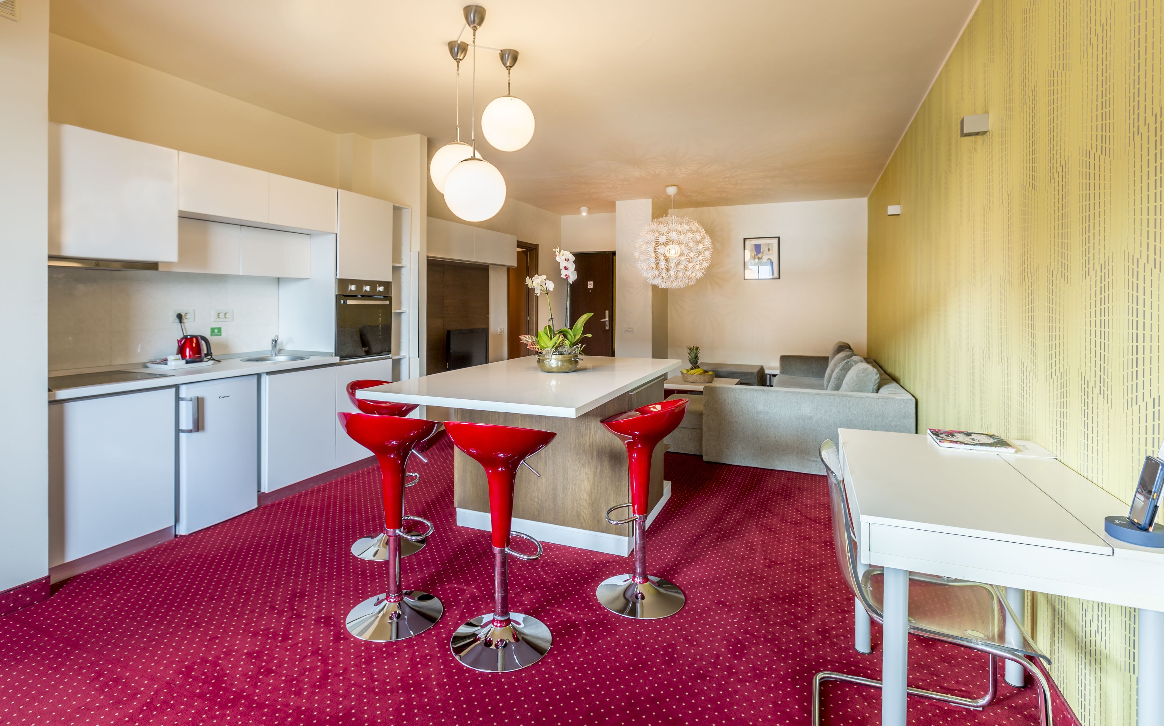 A modern kitchen with white cabinets, a red bar stool area, and a dining table.