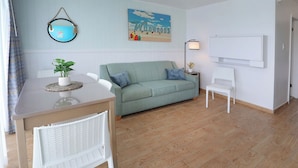 A room with a light green sofa, a white chair, a small table with a plant, a framed picture on the wall, and a whiteboard. - Paradise Oceanfront Resort (Wildwood Crest)