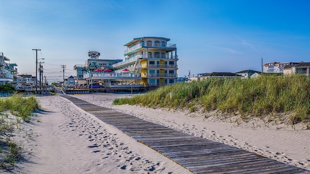 A beachside boardwalk leading to a multi-story building with balconies, a pier, and beachside vegetation. - Paradise Oceanfront Resort (Wildwood Crest)
