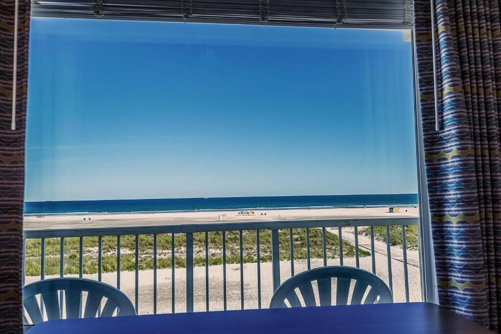 Een kamer met uitzicht op een strand, een raam met gordijnen, en een tafel met stoelen.