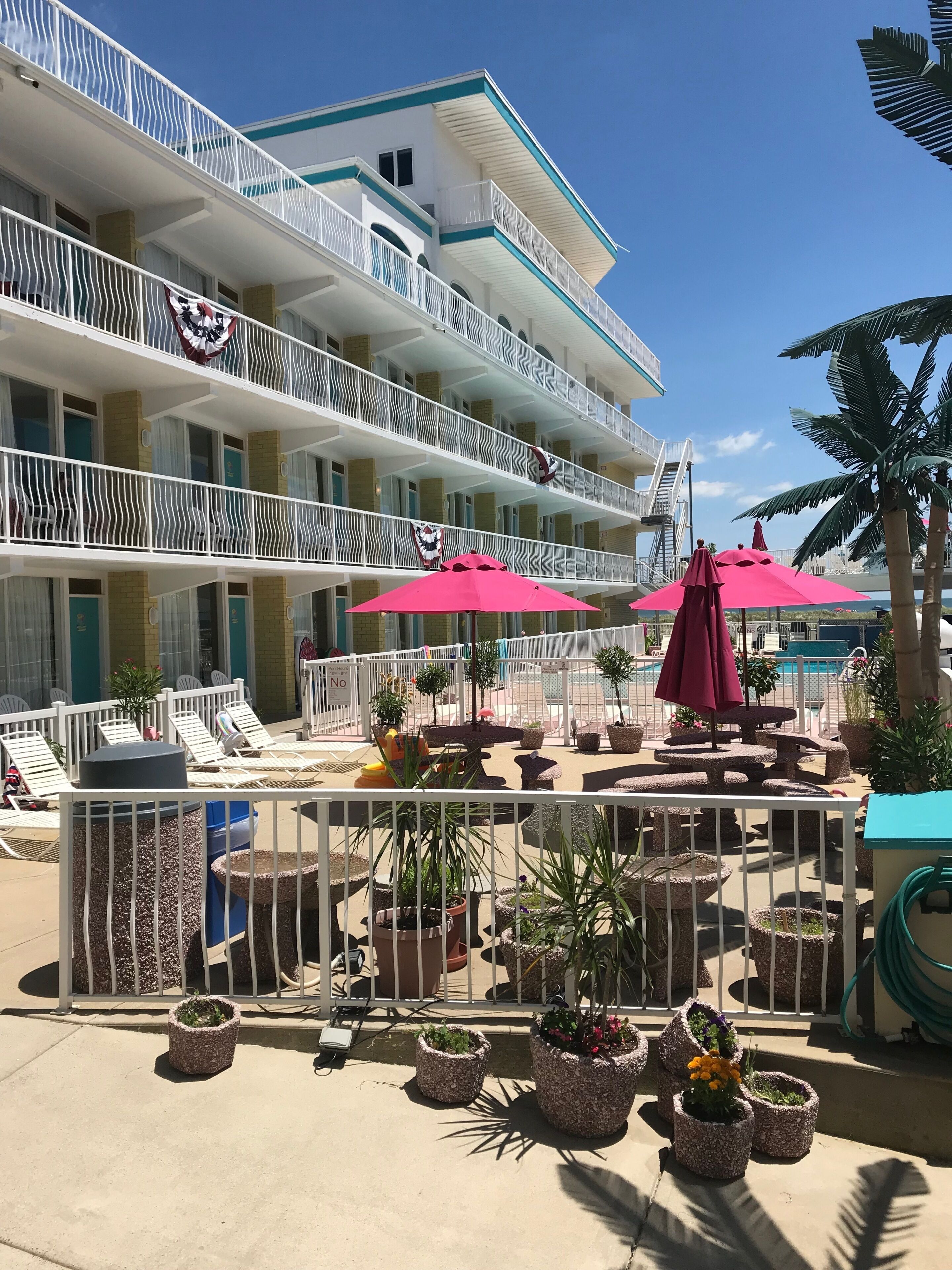 A hotel with multiple balconies, outdoor seating with umbrellas, and potted plants.