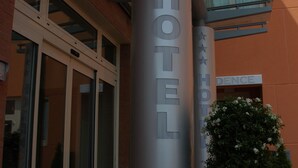 A hotel entrance with a large pillar displaying the name "HOTEL" and stars, a glass door entrance, and a potted plant.