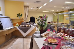 A buffet setup with various food items, a flower arrangement, and a glass display case. - Hotel Tati (Lugo)