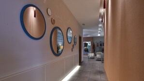 A hallway with a series of circular mirrors on the wall, a tiled floor, and a view into a room with a bed and a chair.
