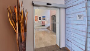 A hotel entrance with a clear glass door, a sign indicating the location of the stairs, and a decorative arrangement of dried plant stalks on the wall.