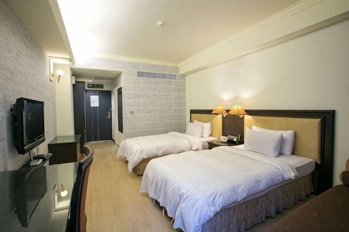A hotel room with two beds, a TV, a desk, and a door leading to a bathroom.