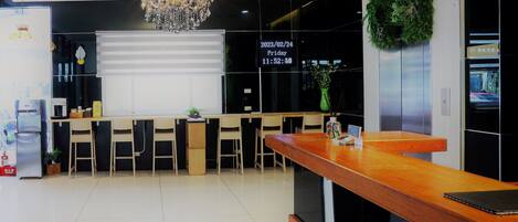 A modern reception area with a wooden reception desk, a chandelier, and a large window with blinds.