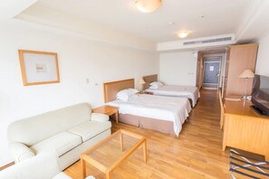 Habitación de hotel con sofá, dos camas individuales, televisión y suelo de madera.
