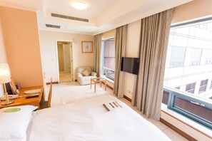 Una habitación de hotel con una cama, un escritorio con lámpara, una silla, un televisor y un ventanal con cortinas.