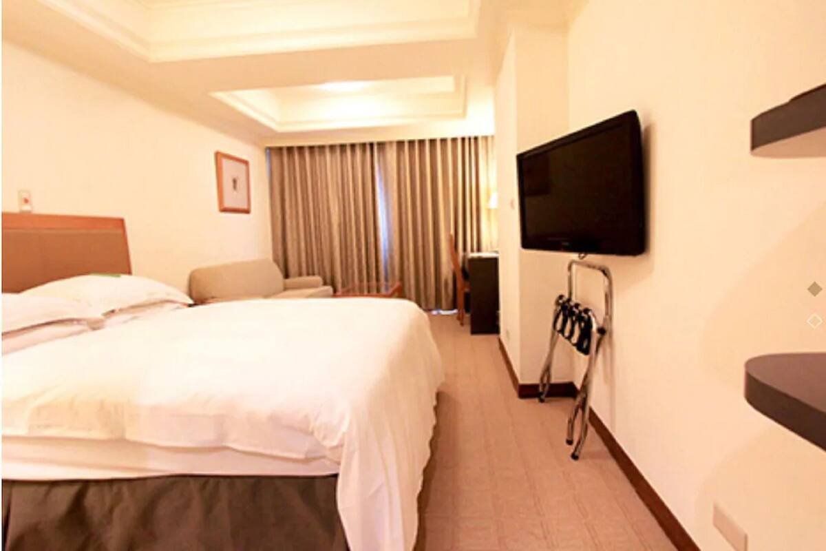 A hotel room with a large bed, a television mounted on the wall, a desk, and a chair.