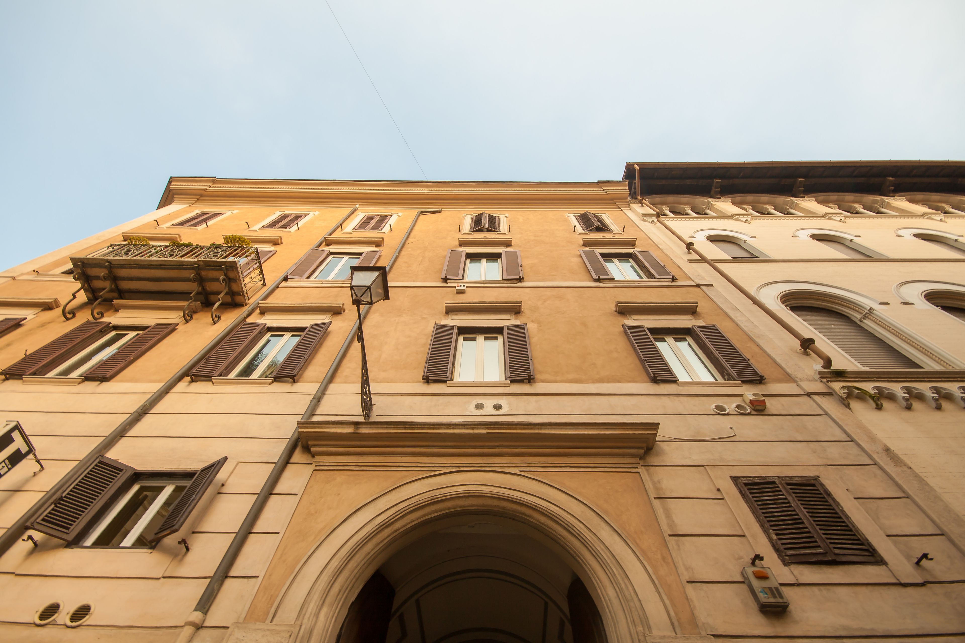 A building with multiple windows, a central archway, and a small balcony with plants.