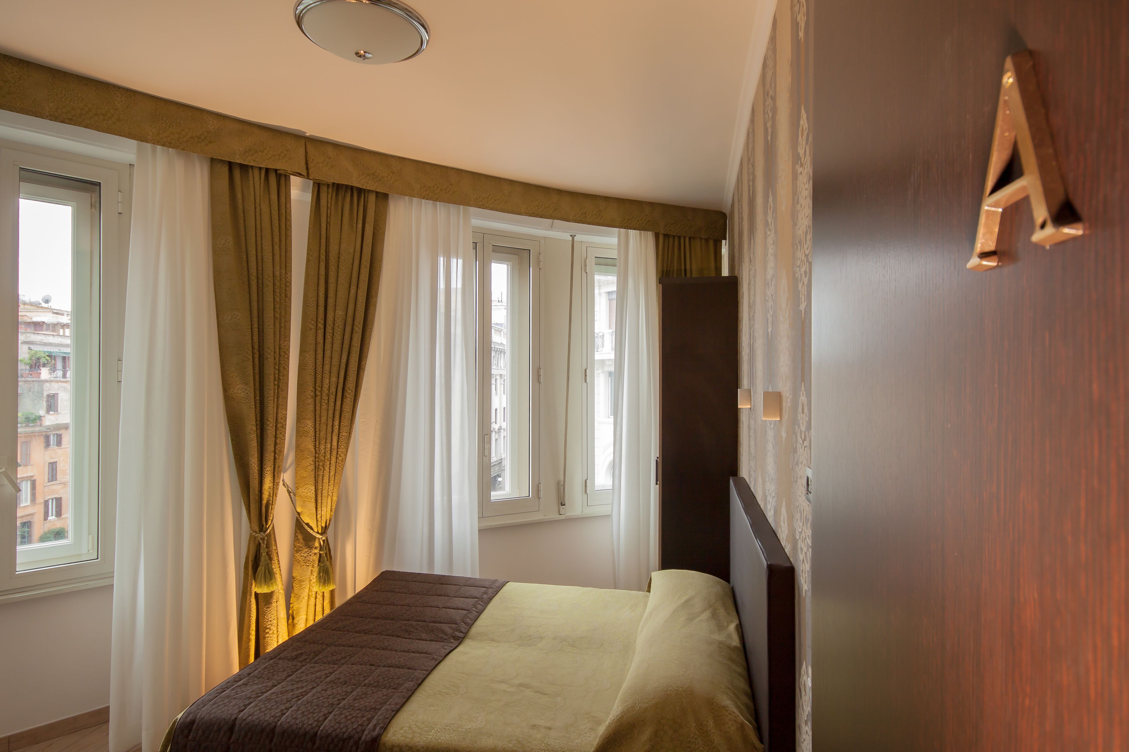 Een hotelkamer met een bed, gordijnen, een houten wand en een raam met uitzicht op gebouwen.