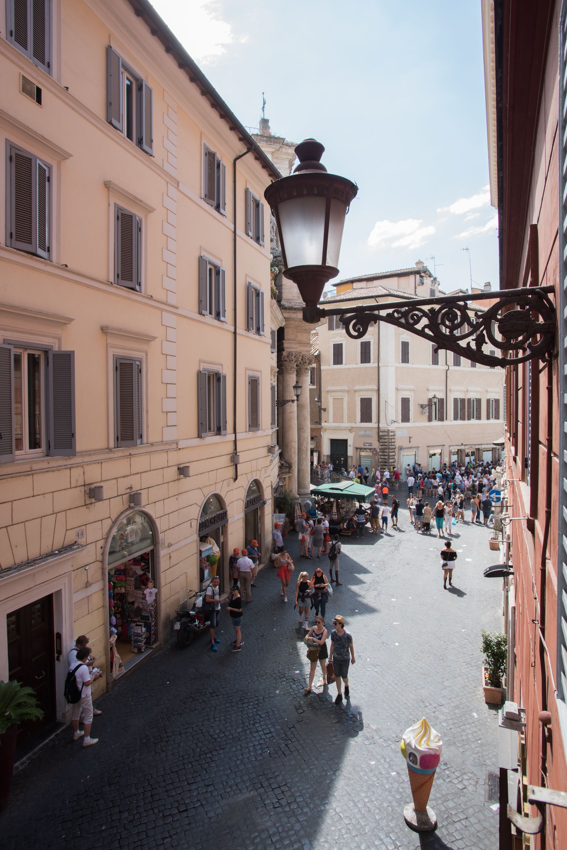 A cobblestone street with pedestrians, historic buildings, and a street lamp.