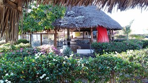 A thatched-roof structure with outdoor seating and a garden area. - Flamingo Villas Resort (Malindi)