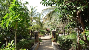 A pathway flanked by lush greenery and palm trees, leading to a shaded area with seating. - Flamingo Villas Resort (Malindi)