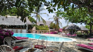 A pool area with lounge chairs and a thatched-roof building. - Flamingo Villas Resort (Malindi)