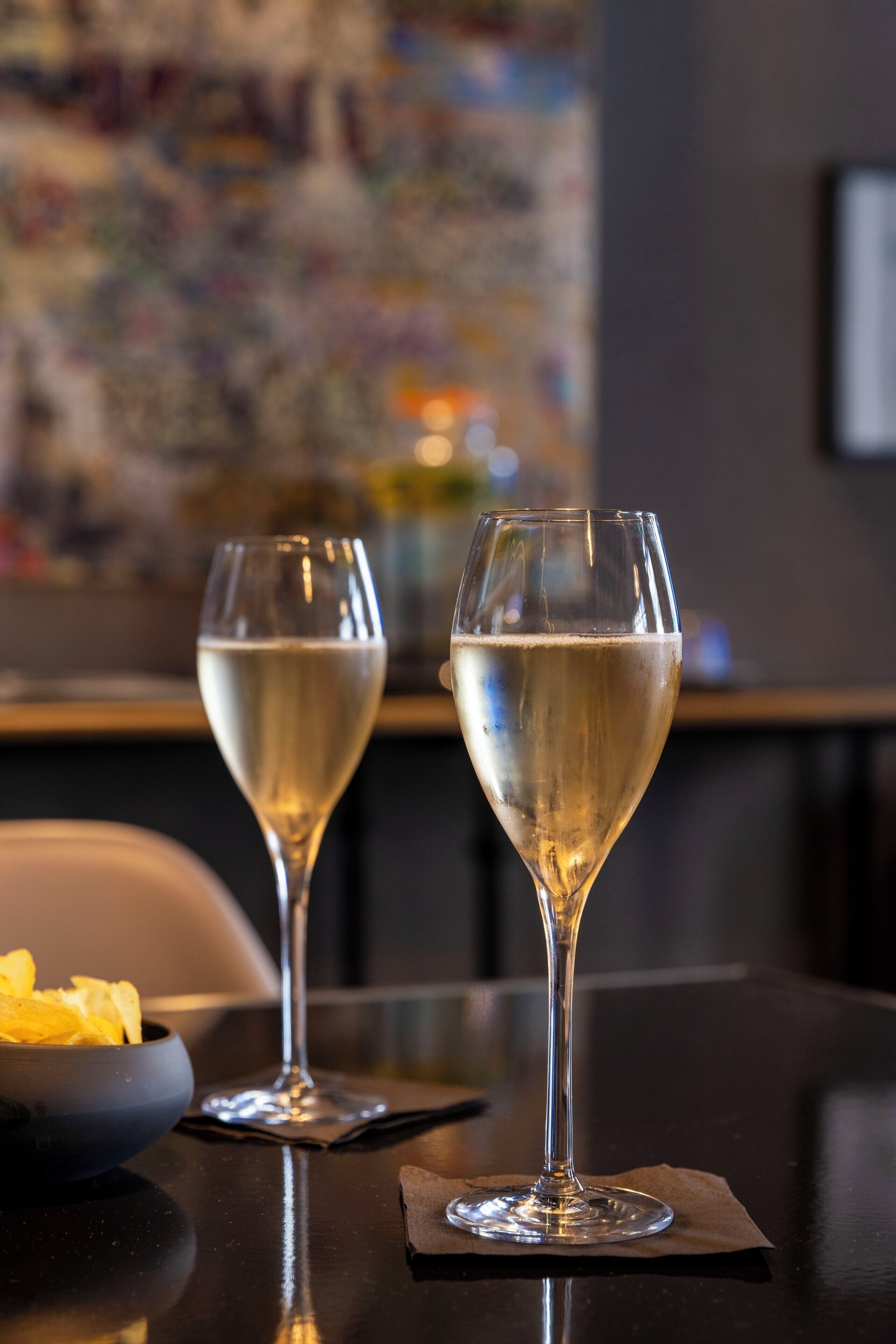 Dos copas de vino blanco sobre una mesa con un bol de patatas fritas.