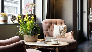 Um espaço de estar acolhedor com uma poltrona confortável, uma pequena mesa com xícara e pires, e um vaso de planta.