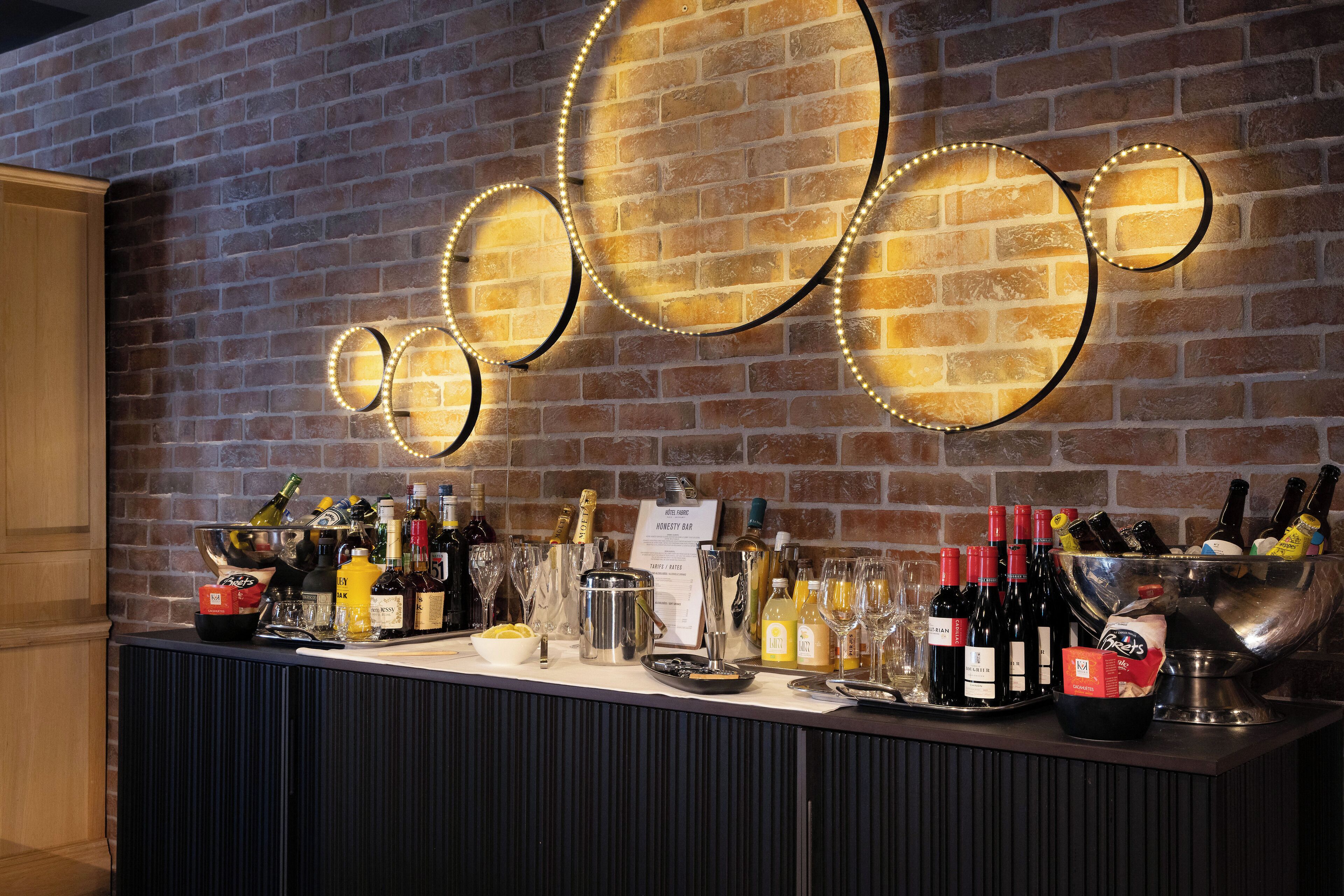 Eine Bar mit Backsteinwand, einer Auswahl an Flaschen, Gläsern und einer Speisekarte.