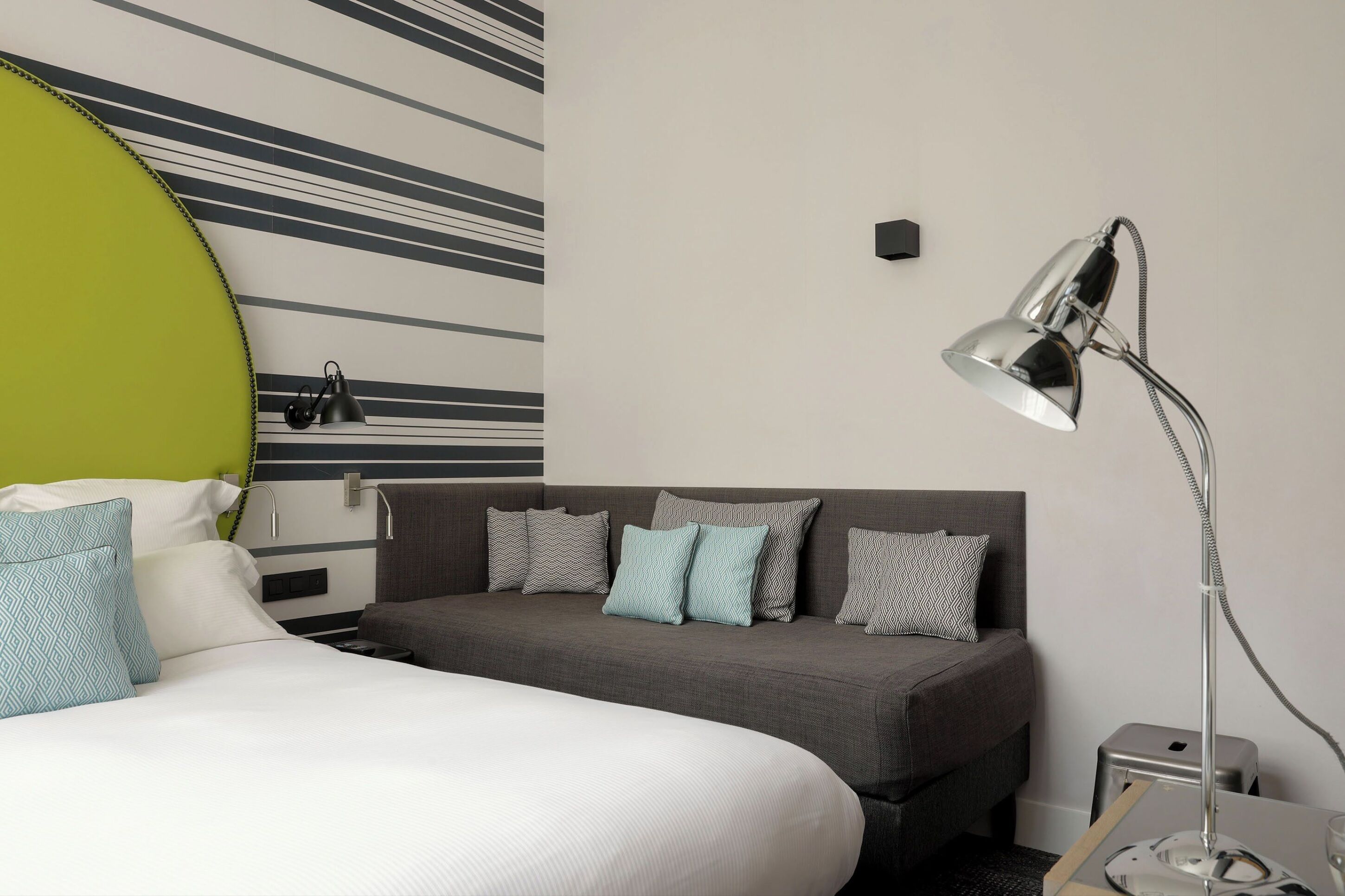 Una habitación de hotel moderna con cama, sofá, escritorio y lámpara.