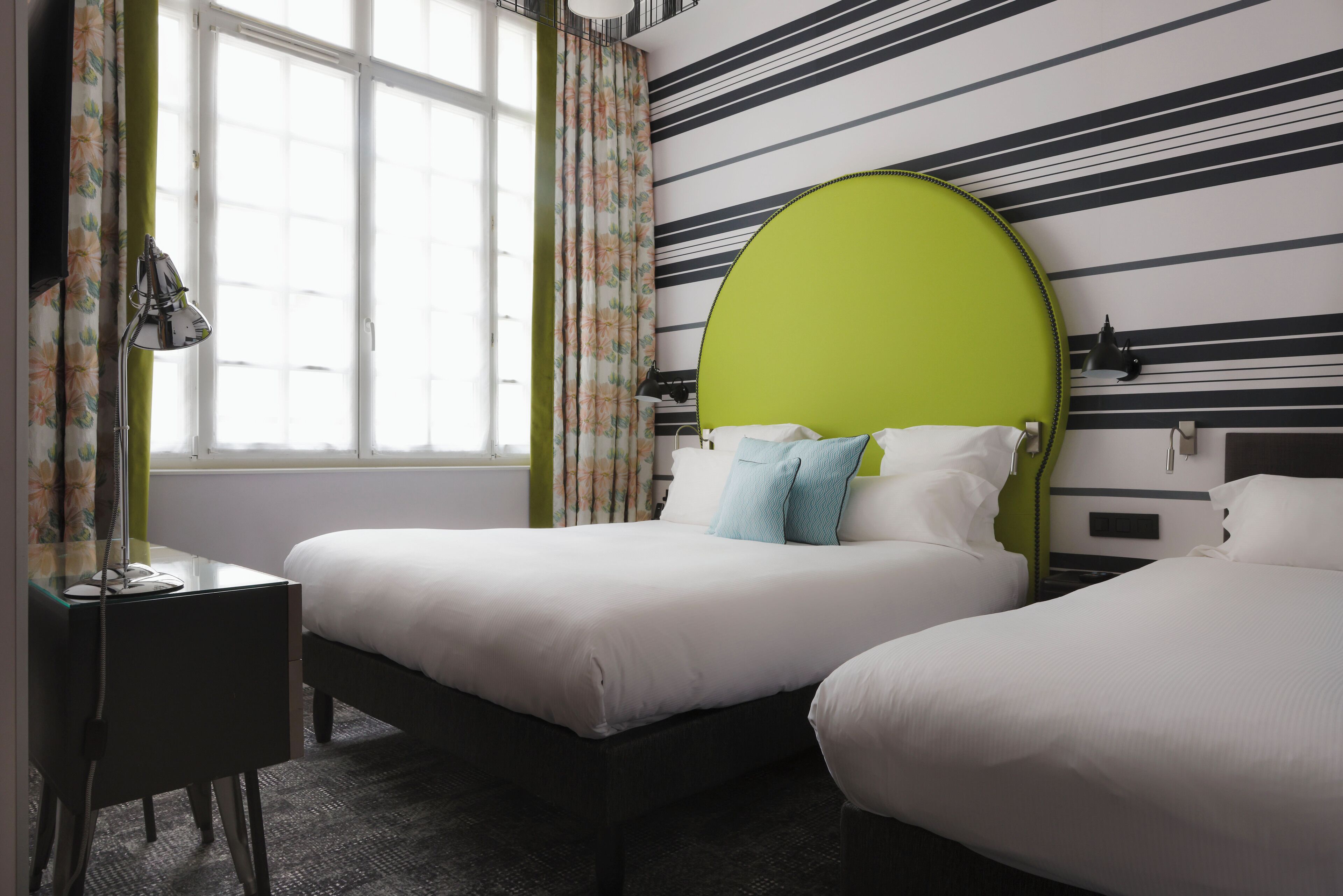 A hotel room with two beds, a desk, and a window with curtains.