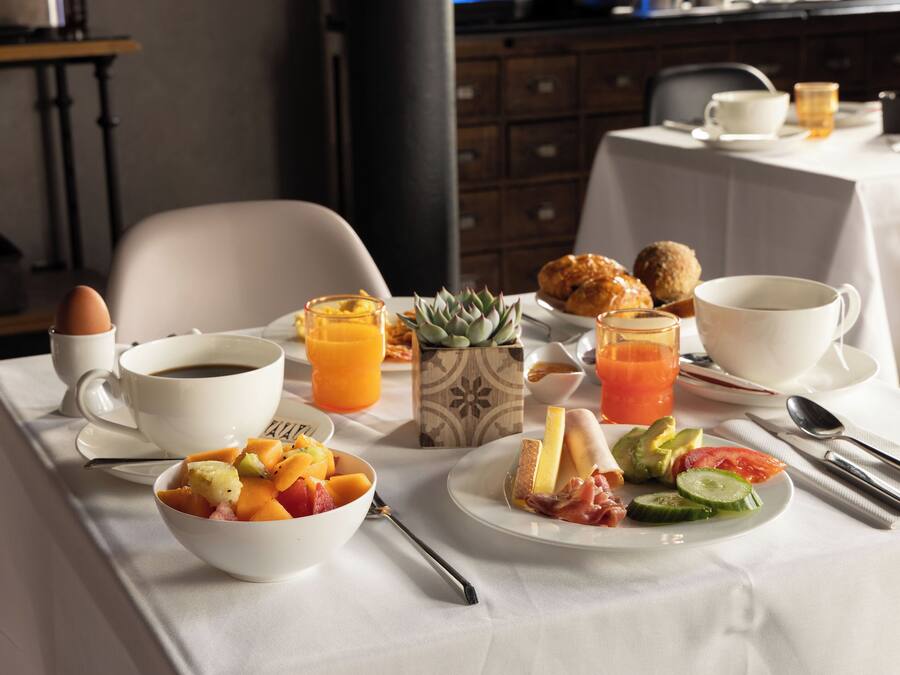 Ein Frühstückstisch mit verschiedenen Speisen, darunter Obst, Gemüse und Gebäck, sowie Tassen Kaffee und Saft.