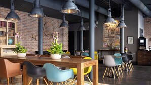 Uma área de refeições moderna com mesa de madeira, cadeiras coloridas e luminárias pendentes em estilo industrial.