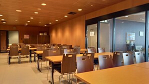 Una sala conferenze con tavoli e sedie multipli, pareti in legno e ampie finestre.