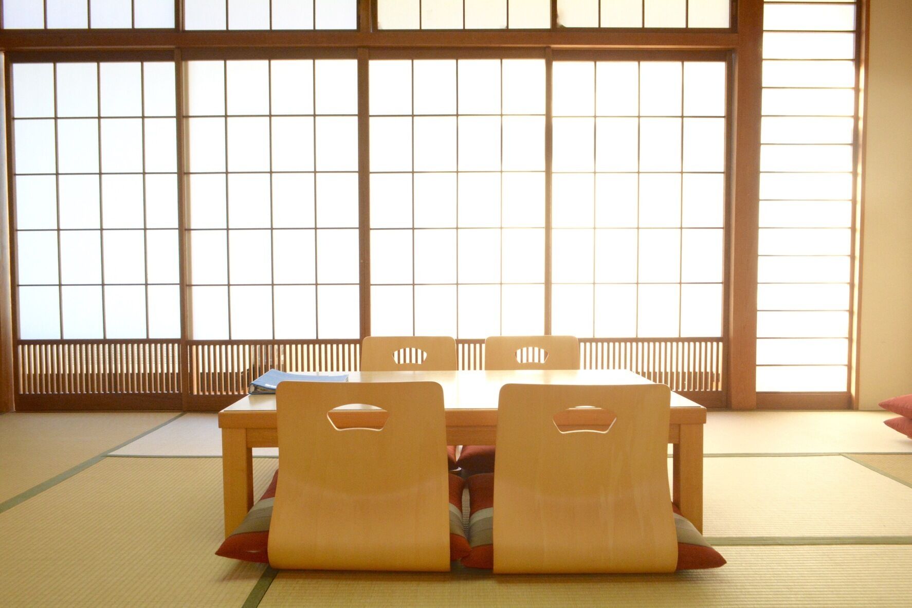 Tatami-mattoilla päällystetty huone, jossa on matala pöytä ja neljä tuolia, suuret shoji-liukuovet ja näkymä ulos.