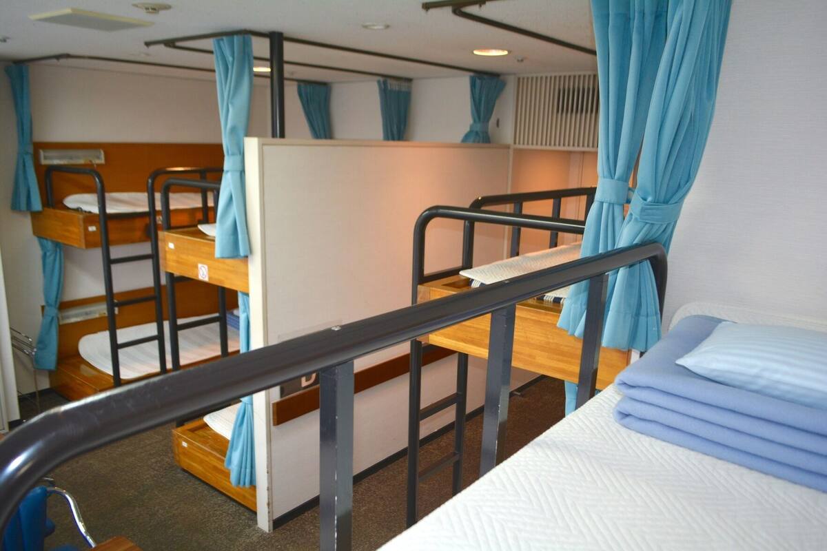 Um dormitório com beliches de madeira, grade de metal e cortinas azuis.