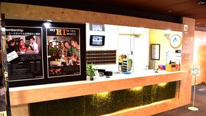 Una reception con un bancone in legno e un elemento decorativo simile al muschio verde. Sul lato sinistro, due manifesti: uno intitolato "Membership" e l'altro "Say HI to the world".