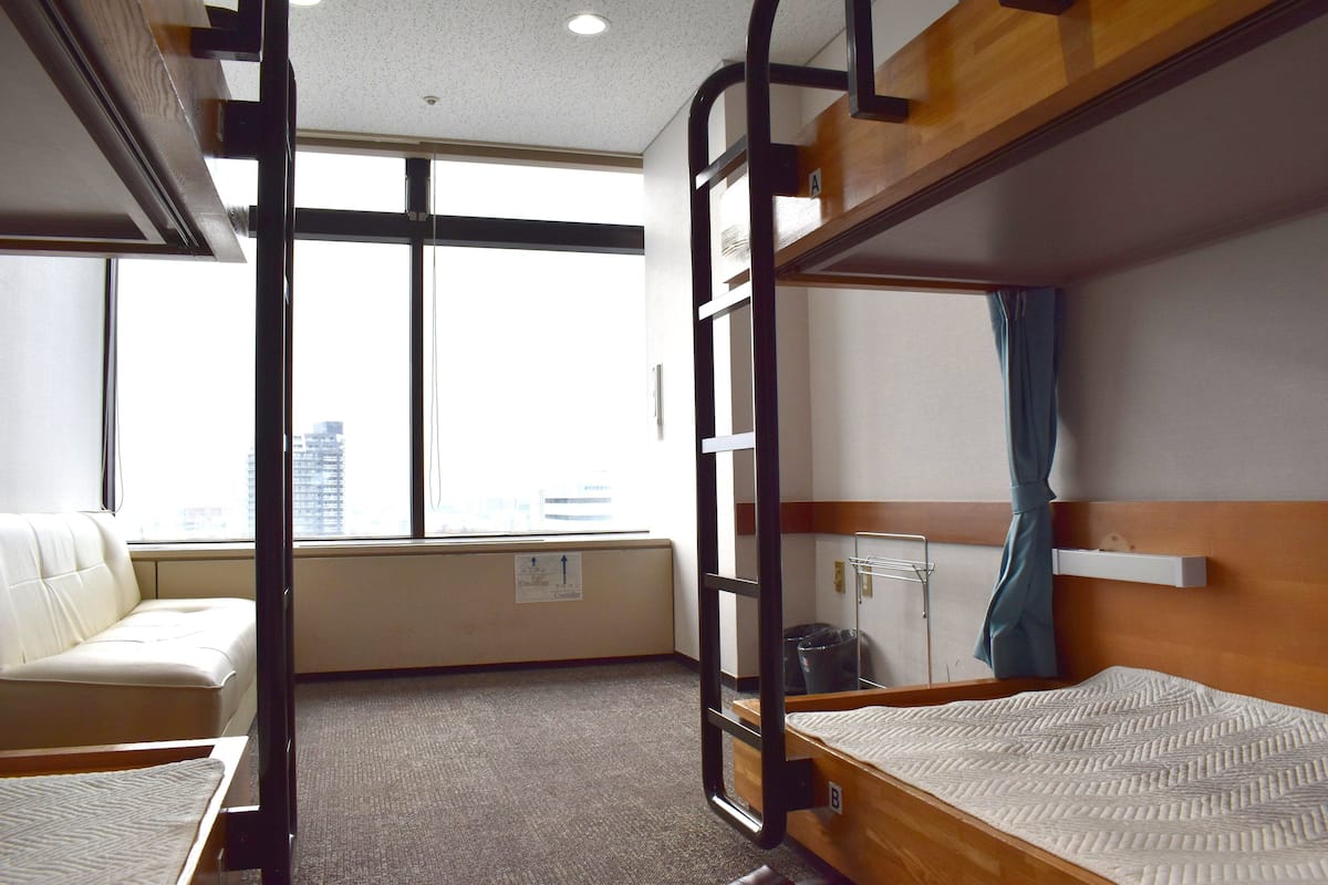 Quarto com beliche, sofá e radiador, além de uma janela.