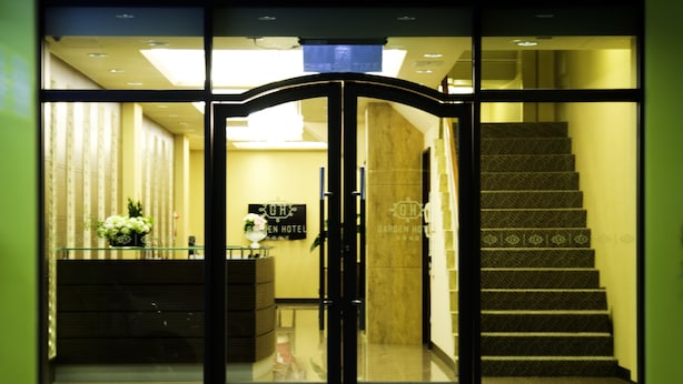 Entrada de hotel con puerta de vidrio, un mostrador de recepción y una escalera que conduce a los pisos superiores.