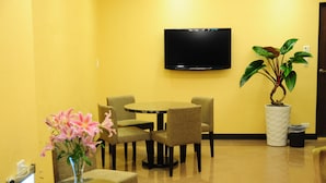 Un vestíbulo de hotel con una mesa redonda, cuatro sillas, un televisor de pantalla plana, una planta en maceta y un jarrón con flores rosadas.