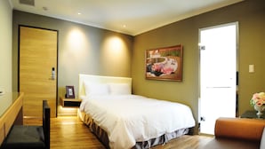 Una habitación de hotel con cama, mesita de noche, banco y una puerta.