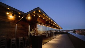 A modern outdoor seating area with wooden walls and a glass enclosure, featuring multiple tables and chairs.