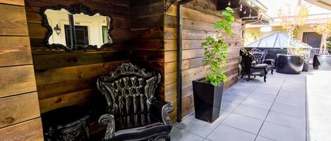 A wooden exterior with a black ornate chair, a potted plant, and outdoor furniture.