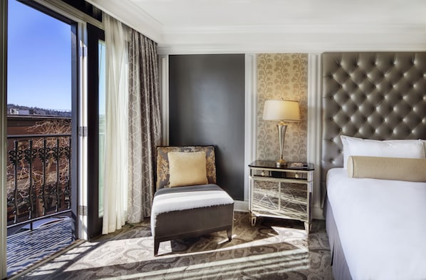 A hotel room with a bed, a chair, a nightstand, a lamp, and a view of the outdoors.