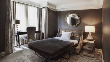 Une chambre d’hôtel avec un grand lit, un bureau, une chaise, un miroir rond et une lampe.